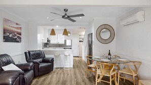 Una sala de estar moderna con un sofá de cuero, una mesa de comedor con sillas, un ventilador de techo y una cocina al fondo.