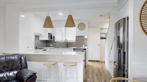 Una cocina moderna con armarios blancos, una isla central con taburetes, iluminación colgante y un refrigerador grande.