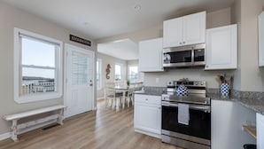 A modern kitchen with white cabinetry, stainless steel appliances, and a view of the outdoors through a large window. - Amazing 10 Bedroom Compound on the Water with 6 Bedroom Home & 4 Studio Cottages (Stonington)