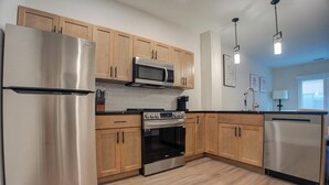 A modern kitchen with stainless steel appliances, wooden cabinets, and a black countertop. - Landing | Chic 1BD, Clubhouse, Rooftop Lounge (Philadelphia)