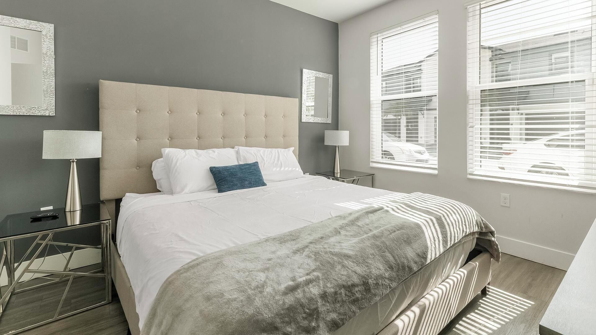 A modern hotel room with a large bed, two bedside tables, and a view of the street through the windows.