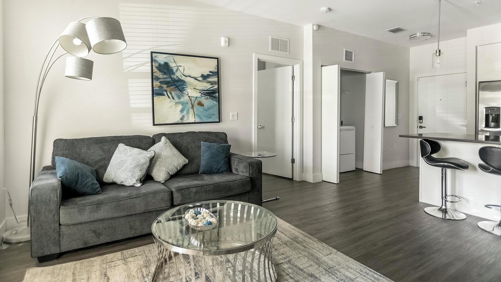 Een moderne woonkamer met een grijze bank, een glazen salontafel en een moderne vloerlamp.