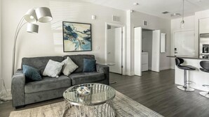 A modern living room with a grey sofa, a glass coffee table, and a contemporary floor lamp. - Landing | Modern 2BD, Gym, Pool (Tampa)