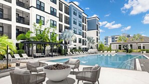 A modern hotel pool area with lounge chairs, a fire pit, and a covered seating area. - Landing | Modern 2BD, Gym, Pool (Tampa)