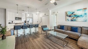 Un appartement moderne comprenant une cuisine, un coin repas et un salon. Il est équipé d’un bar avec des tabourets, d’un canapé et d’une table basse.