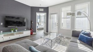 A modern living room with a flat-screen TV, grey sofas, a glass coffee table, and a large window with blinds. - Landing | Incredible 3BD, Gym, Clubhouse (Tampa)