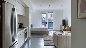 A modern kitchen with a refrigerator, stove, and cabinets. There is a bed with a window and a TV in the living area.