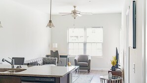 Une cuisine moderne dotée d’un îlot central, d’un coin repas avec une table en verre et d’un espace détente avec un fauteuil.