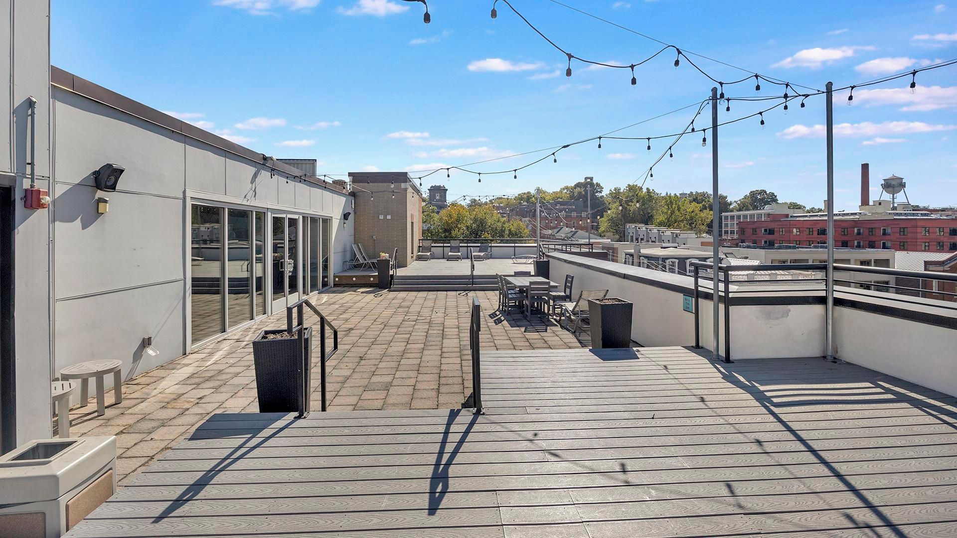 A rooftop terrace with outdoor seating, a trash bin, and string lights.