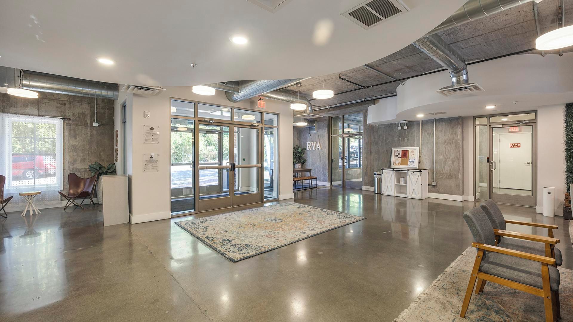 A spacious lobby with a polished concrete floor, a patterned rug, and a reception desk.
