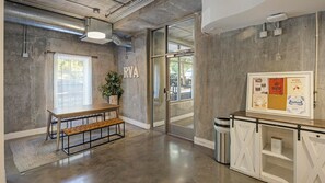 A reception area with a bench, a potted plant, a glass door, and a bulletin board with various notices.