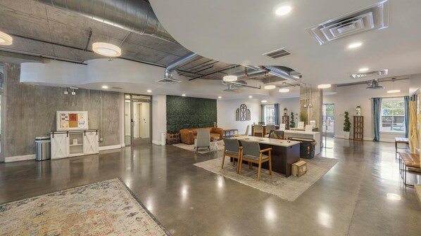 A spacious, modern interior with a central dining area, a reception desk, and a green accent wall.