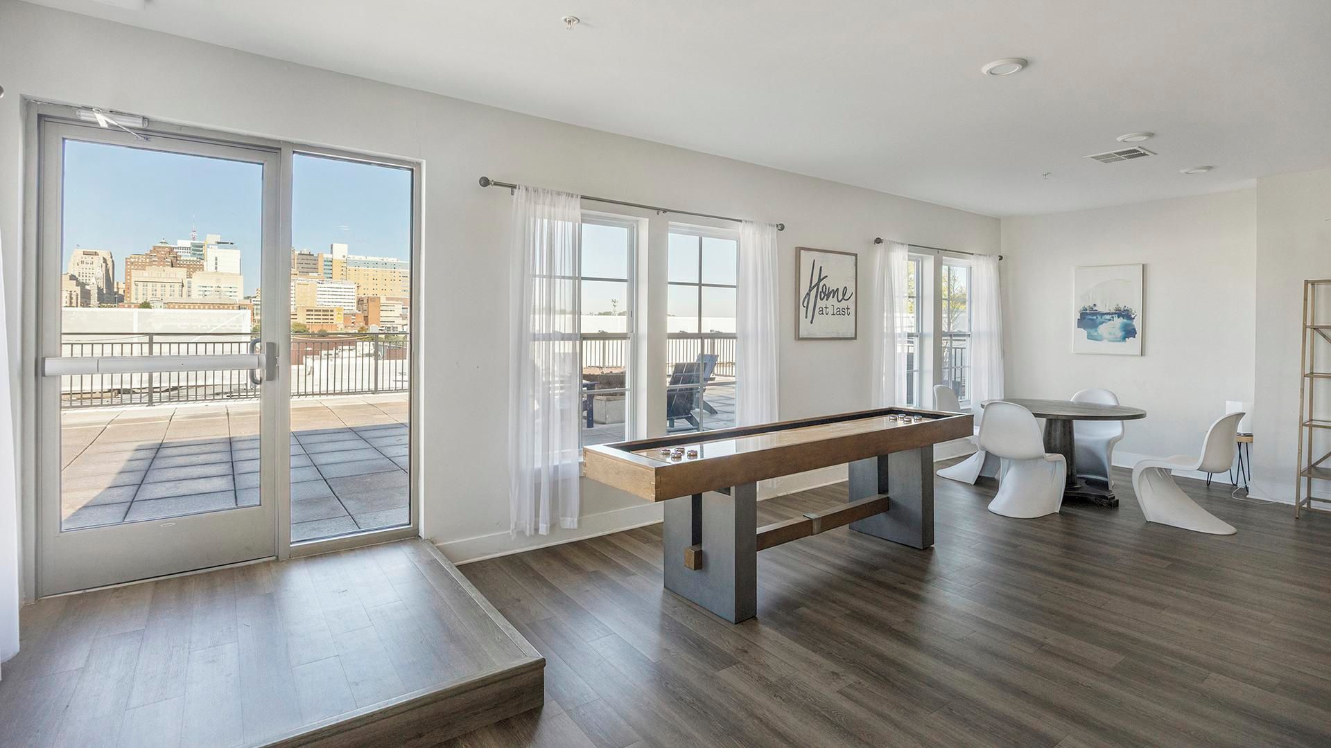 A spacious room with a pool table, a dining area with chairs, and large windows offering a city view.