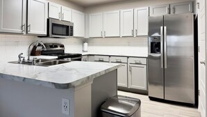 Una cocina moderna con armarios blancos, electrodomésticos de acero inoxidable, encimera de mármol y horno empotrado.