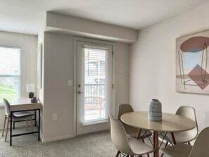 Une pièce comprenant une table à manger et des chaises, une porte avec des stores et un tableau abstrait encadré accroché au mur.