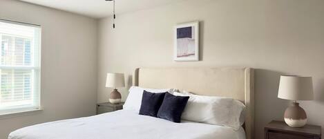A neatly made bed with white and dark blue pillows, a ceiling fan, and two bedside tables with lamps.