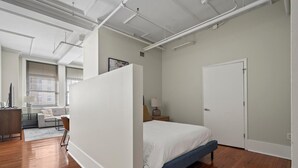Un dormitorio moderno con una cama grande, un escritorio y una silla en una habitación luminosa con pisos de madera y paredes blancas.
