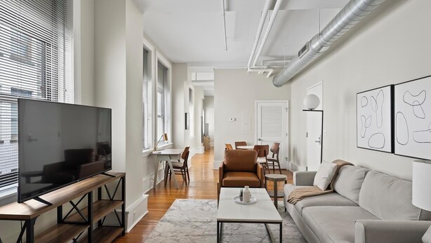 A modern living room with a flat-screen TV, a sofa, a coffee table, and a dining area with chairs and a table.