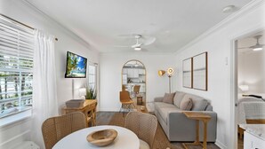 Un salon moderne avec un canapé gris, une table à manger entourée de chaises en osier, un téléviseur à écran plat et un ventilateur de plafond.