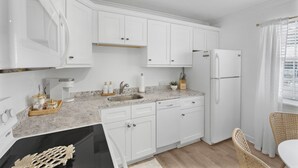 Une cuisine moderne avec des meubles blancs, un plan de travail en granit, un lave-vaisselle encastré et un réfrigérateur.