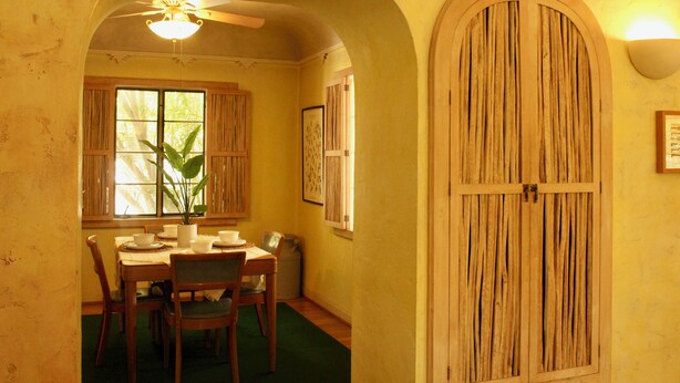 Un coin repas avec une table et des chaises en bois, un ventilateur de plafond et une grande porte en bois.