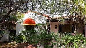 Une maison avec un auvent rouge et jaune, entourée de verdure et bordée d’un chemin en pierre.