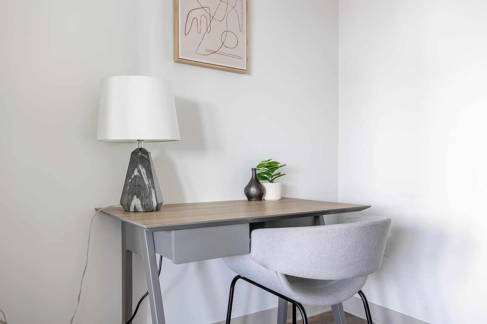 A modern desk with a lamp, a chair, and a small plant on a white wall.