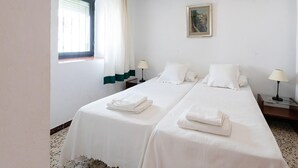 Ein Hotelzimmer mit zwei Betten, weißer Bettwäsche, einem Bild an der Wand und einem Fenster mit Vorhängen.