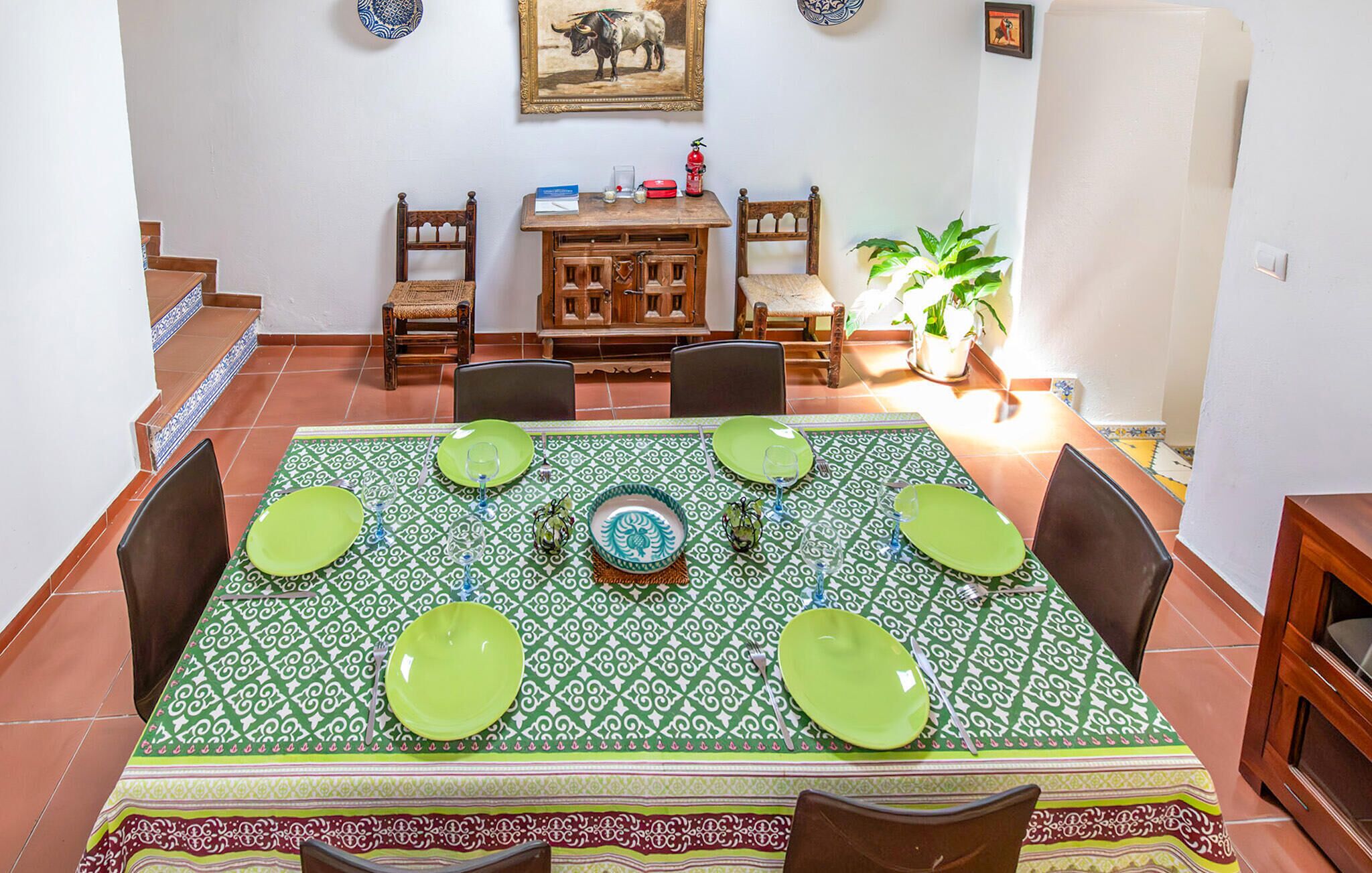 A dining area with a green patterned tablecloth, wooden chairs, and a central decorative plate.