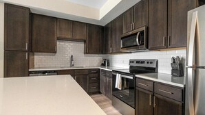 A modern kitchen with dark wood cabinets, a stainless steel refrigerator, a microwave, and an oven.