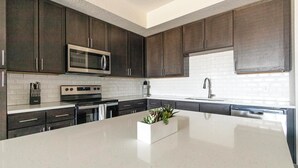 A modern kitchen with dark cabinetry, stainless steel appliances, and a white countertop. - Landing | Stylish 2BD, Pool, Clubhouse (Palmetto)