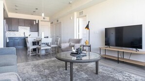 A modern living room with a glass coffee table, grey sofa, and a flat-screen TV. - Landing | Stylish 2BD, Pool, Clubhouse (Palmetto)