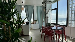 A room with a large window overlooking the sea, a dining area with red chairs, and a white sofa. - 2 Manolo Pris Studio Private Terrace (El Pris)