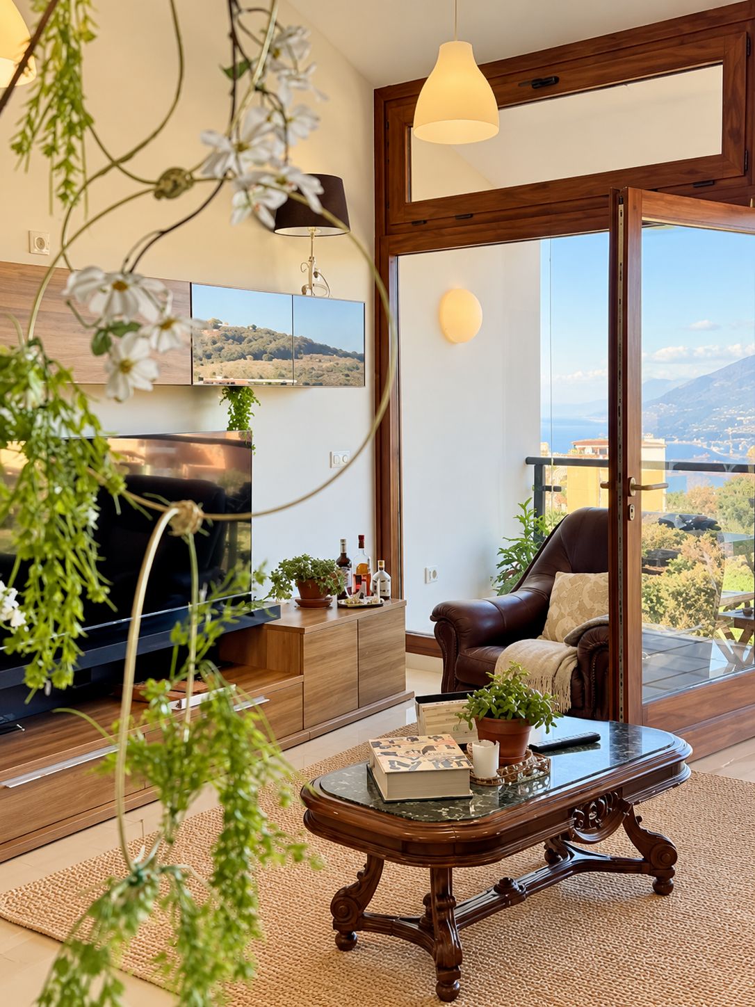 Un salon moderne doté d’un téléviseur à écran plat, de meubles en bois, d’un fauteuil en cuir et d’un balcon avec vue.
