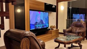 Una sala de estar moderna con un televisor de pantalla plana grande, sillones de cuero, una mesa de centro de madera e iluminación colgante.