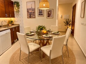 A modern dining area with a glass table, white chairs, and a central plant.