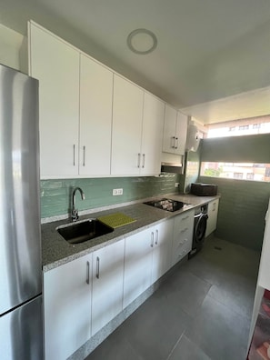A modern kitchen with white cabinets, a stainless steel refrigerator, a built-in oven, a microwave, and a washing machine.