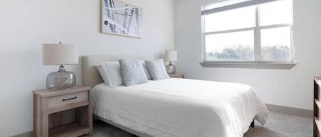 A bedroom with a bed, two nightstands, a window, and a wall-mounted abstract painting.