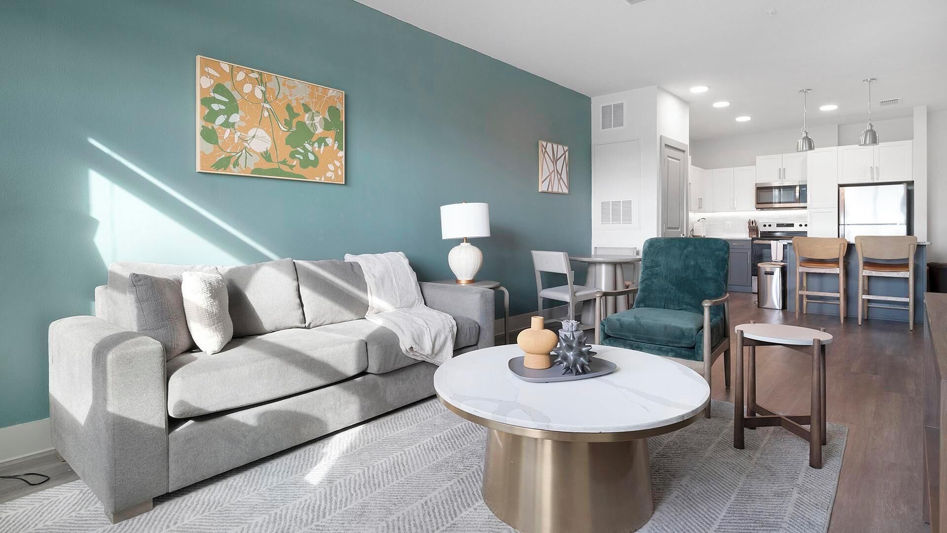 Una sala de estar moderna con un sofá gris, una mesa de centro redonda y un sillón verde azulado.