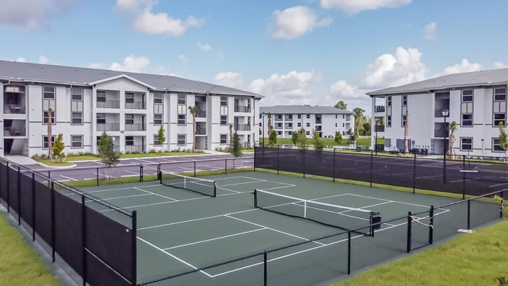 Ein Tennisplatz, umgeben von modernen Mehrfamilienhäusern mit Balkonen.