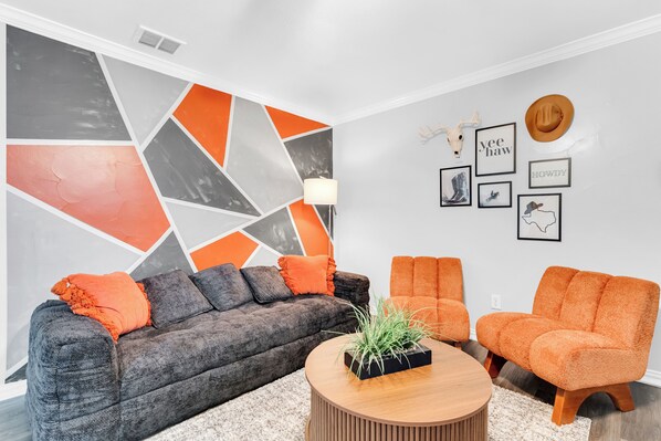 A modern living room with a grey sofa, orange armchairs, and a geometric wall design.