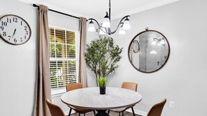 A dining area with a round table, chairs, a potted plant, a chandelier, and a window with blinds. - • NEW • Walk to AT&T Stadium  and Globe Life Field • Rangers • Free parking (Arlington)