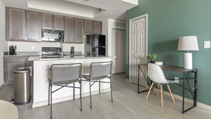 Una cocina moderna con una isla central, taburetes de bar, una mesa de comedor con sillas y un cubo de basura.