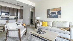 Una sala de estar moderna con un sofá, sillas, una mesa de centro y una cocina al fondo.