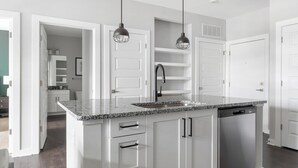 A modern kitchen with white cabinetry, a granite countertop, a built-in dishwasher, and pendant lighting.