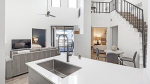 A modern apartment with a kitchen, dining area, and living room. It features a large window, a ceiling fan, and a staircase.