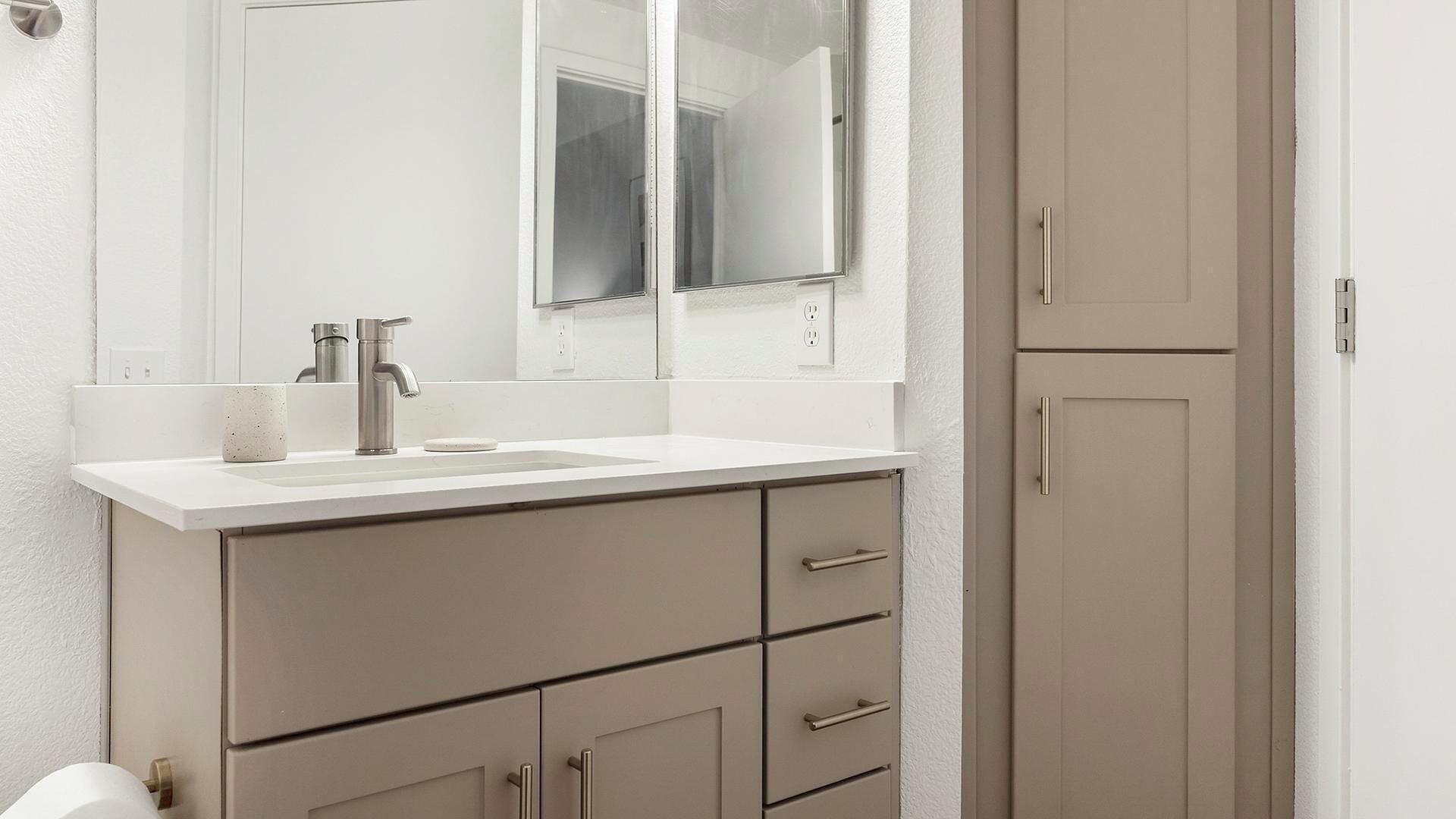 A bathroom with a white sink, a mirror, and beige cabinets.