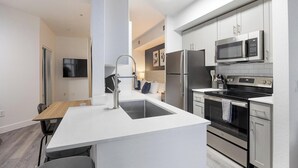 A modern kitchen with a central island, stainless steel appliances, and a flat-screen TV in the background.