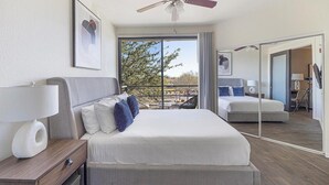 Une chambre d’hôtel moderne dot ée d’un grand lit, d’un bureau avec une lampe, d’un ventilateur de plafond et d’une grande fenêtre donnant sur l’extérieur.