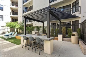 An outdoor patio with a grill, bar stools, and a covered seating area. - Landing | Amazing 1BD, Yoga Studio, Gym (Tempe)